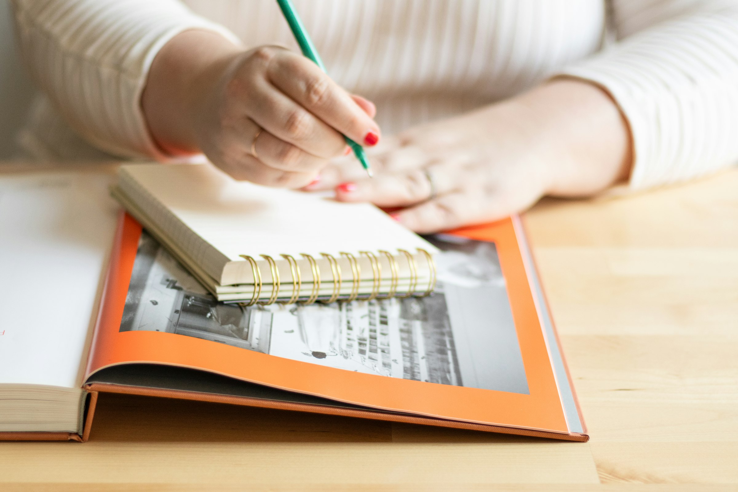 Hands writing in a notebook beside a reference book on a desk