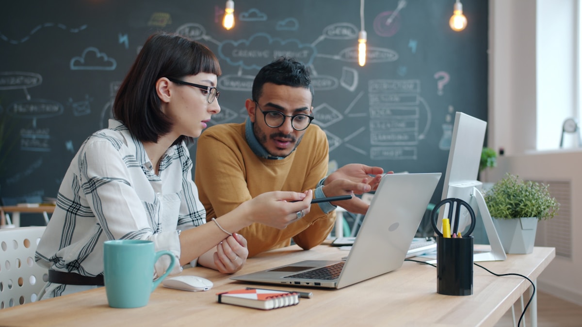 Two developers pairing at a laptop in front of a brainstorm board, reading a JWT and writing a guard clause